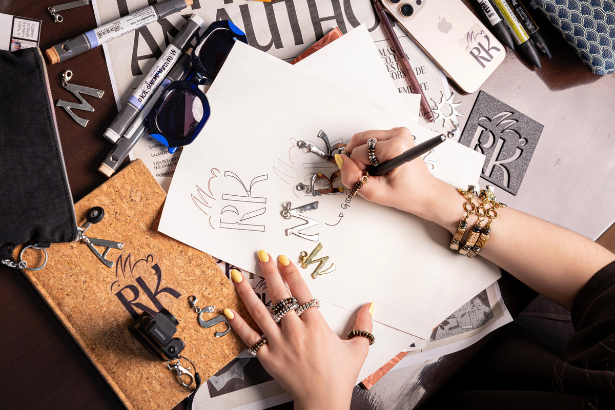 Mano dibujando letras, con anillos y pulseras RONNIKA